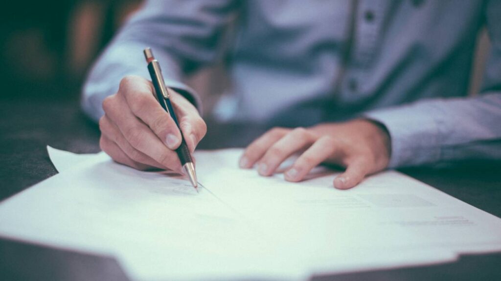 A professional man signing a contract, looking intently at the paper on the desk before him.