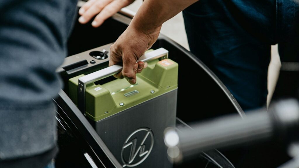 Person lifting a removable electric scooter battery from the battery compartment