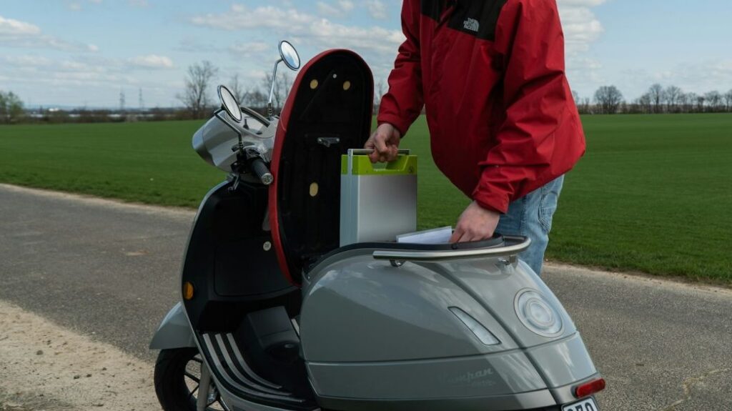 An orange electric scooter parked against a stone wall with text asking about removable batteries in electric scooters.