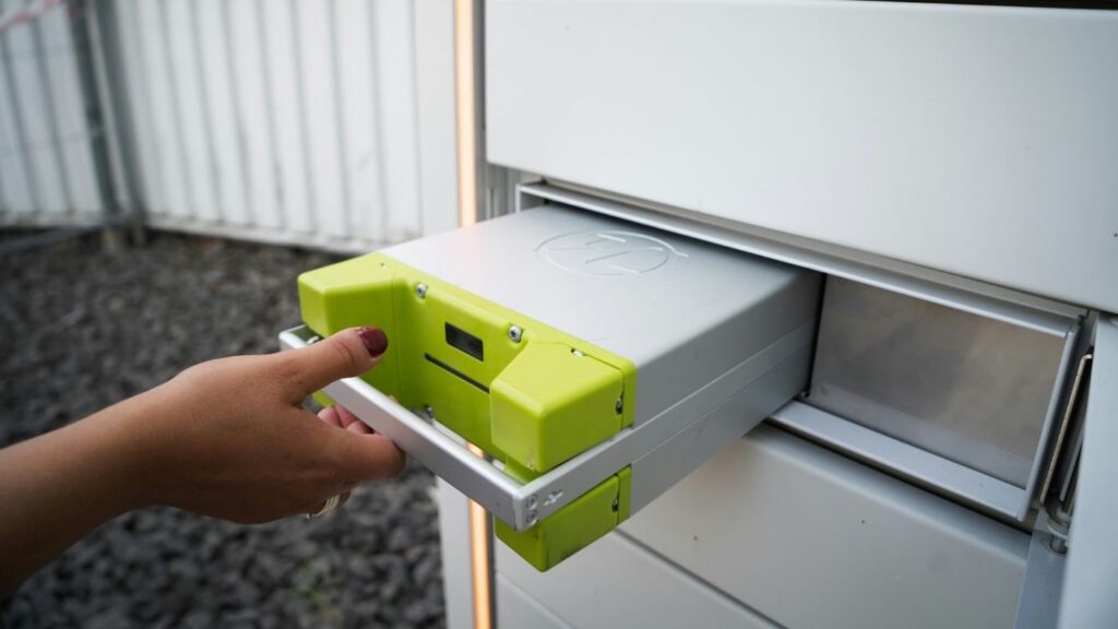 Hand removing a modular electric scooter battery from a charging station